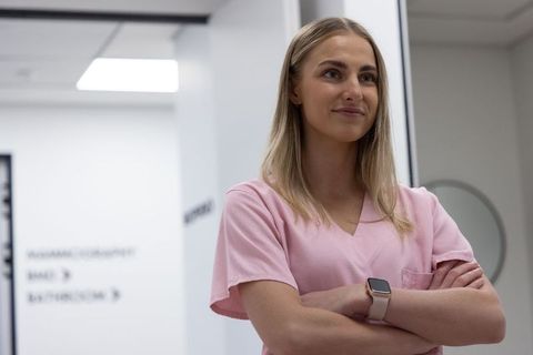 Confident nurse standing in modern clinic corridor wearing pink scrubs and smartwatch