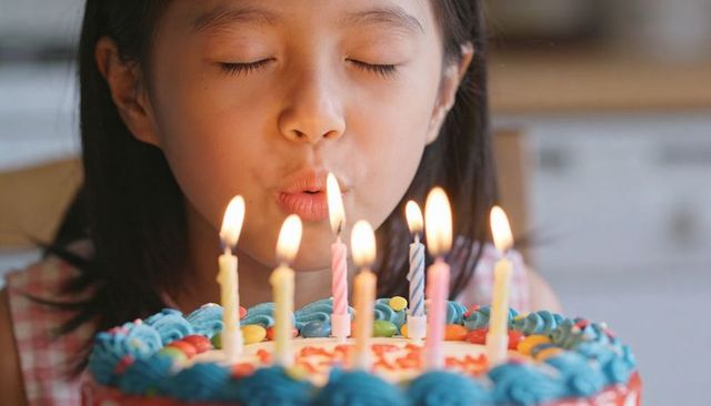 Asian girl blowing birthday candles on colorful blue frosted cake with candy decorations