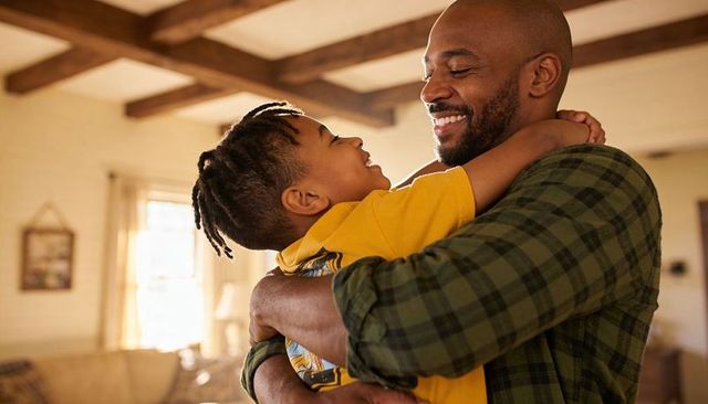 Father embracing smiling son in cozy living room, cradling child, family bond