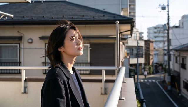 Contemplating asian woman standing on rooftop balcony in sunlit urban neighborhood