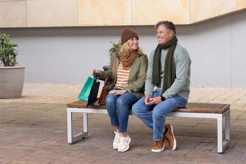 Mature couple taking shopping break on urban bench wearing casual fall scarves and sneakers