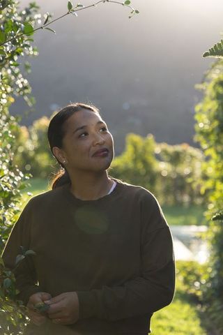 Mid-adult asian woman standing in backlit garden corridor at golden hour, contemplative portrait