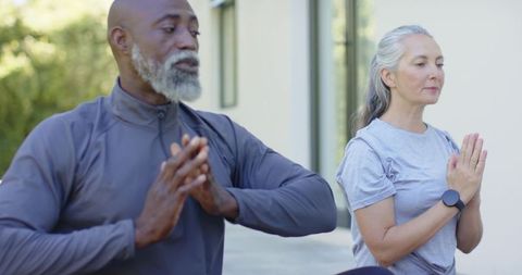 Senior couple practicing mindful meditation on sunlit patio in activewear with smartwatch