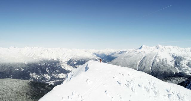 Hikers standing atop a snow-covered mountain under a clear blue sky offers a stunning panoramic view of the surrounding snow-blanketed landscape. This can be used for winter adventure travel promotions, outdoor lifestyle magazines, nature exploration blogs, and winter sports advertisements.