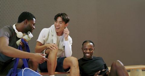 Diverse male basketball teammates laughing and relaxing on bench after game, casual camaraderie