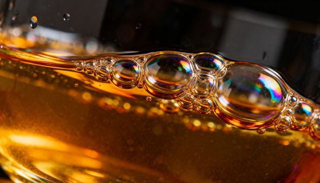 Macro floating iridescent bubble chain in warm amber liquid inside curved glass close-up