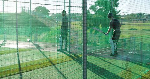 Cricket batter practicing in sunlit netted cage swinging bat during outdoor training