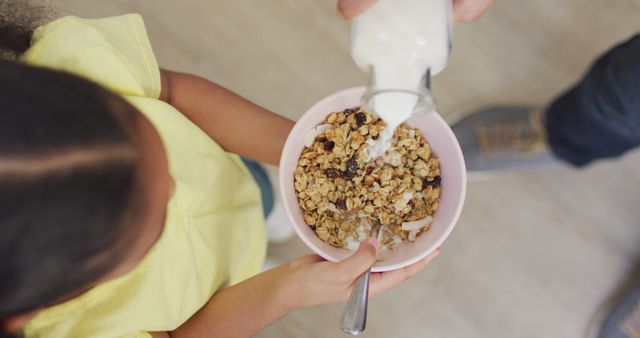 Child enjoying healthy breakfast with fresh milk poured on cereal in a bowl. Ideal for use in advertisements, blog articles, and social media promoting nutritious eating habits and morning routines for children.