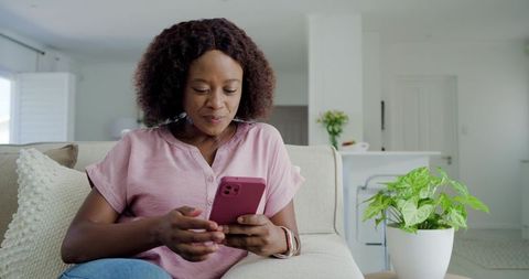 Woman checking smartphone on sofa in bright modern living room wearing smartwatch and denim