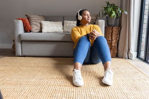 African american woman relaxing on rug with headphones enjoying bright cozy living room