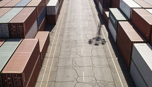 Stretching cracked roadway through container terminal with crane shadow