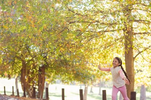 Laughing girl balancing in autumn park under golden trees