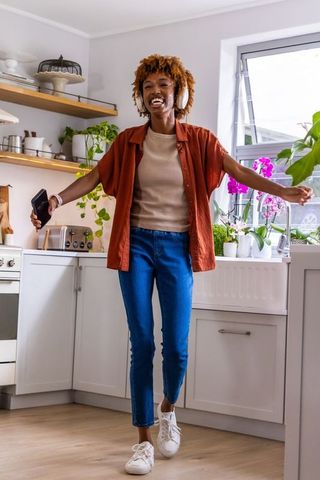 Happy african american woman dancing in modern kitchen, listening on wireless headphones
