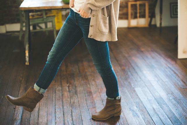 Photo capturing person wearing denim jeans and ankle boots, walking indoors on wooden floor. Suitable for lifestyle blogs, fashion websites, autumn fashion promotions, and advertisements targeting casual and trendy clothing. Great for illustrating everyday comfort and style.