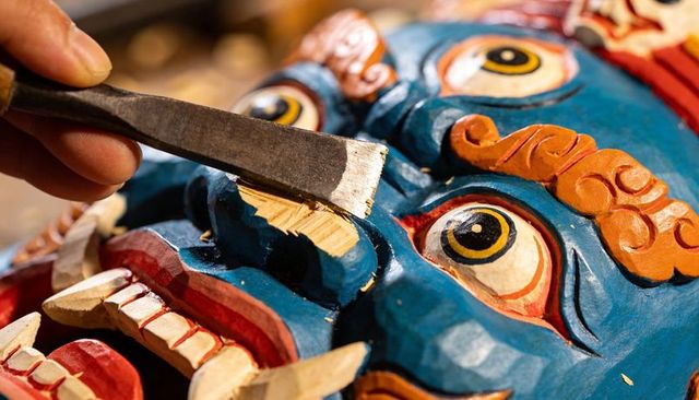 Artisan carving traditional blue ceremonial mask with chisel close-up detail