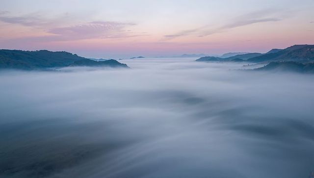Misty mountain valleys filling with morning fog and pastel sunrise sky — serene panorama