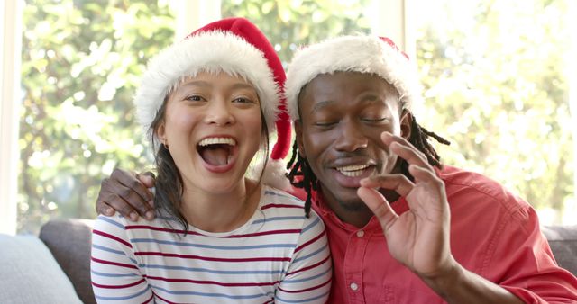 Two friends wearing Santa hats and showing joyful expressions while celebrating Christmas together. The diverse duo exudes happiness and festivity, making this perfect for holiday cards, festive advertisements, or social media campaigns promoting unity and joy during the holiday season.