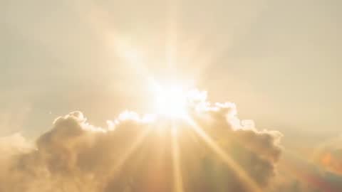 Sunburst rising behind cumulus crest, casting golden rays and lens flare over horizon