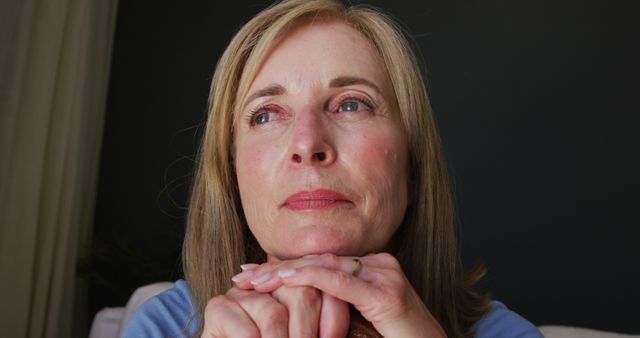 Mature woman resting chin on hands, reflecting in quiet moment. Useful for illustrating concepts of introspection, contemplation, emotional depth. Could be used in articles or content about aging, mental health, personal reflections.