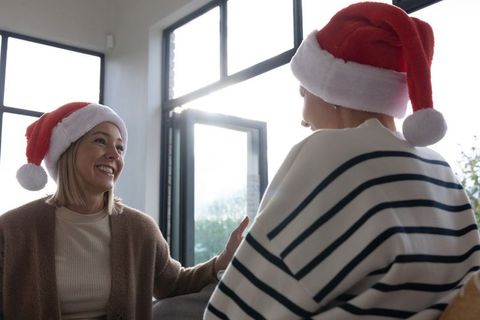 Friends chatting in living room wearing santa hats smiling holiday cheer cozy backlit interior