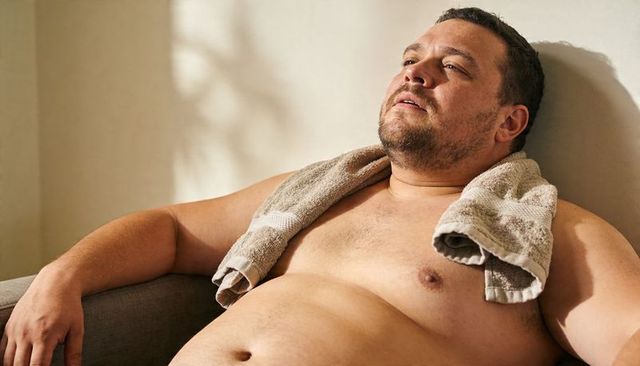Relaxed middle-aged man reclining on sofa with towel, sunlit home recovery and rest