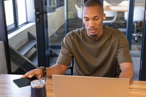 African american professional working on laptop in coworking space reaching for phone