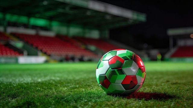 Resting multicolor soccer ball gleaming on floodlit stadium grass at night