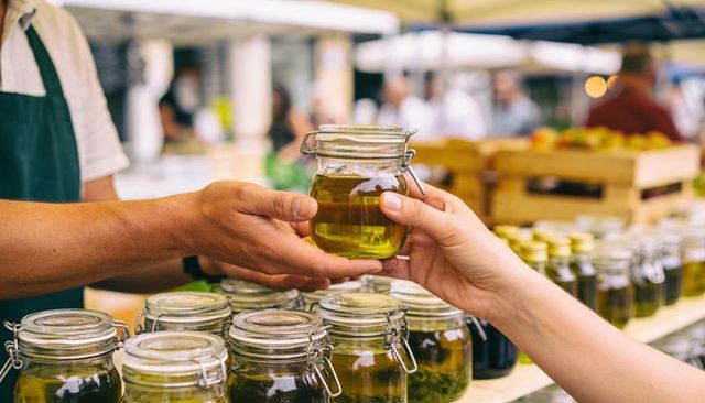Vendor and customer exchanging glass jar of olive oil at outdoor farmers market