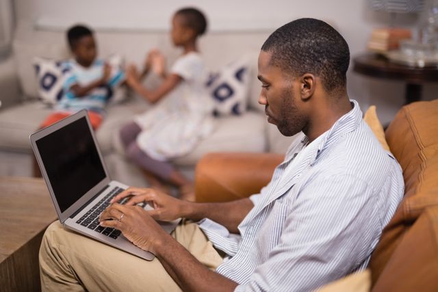 Side view of young man using laptop while children playing at home