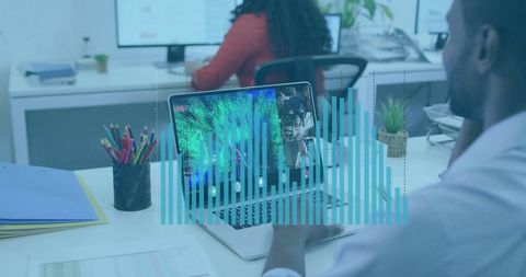 Man Analyzing Digital Charts on Laptop in Open-Plan Office