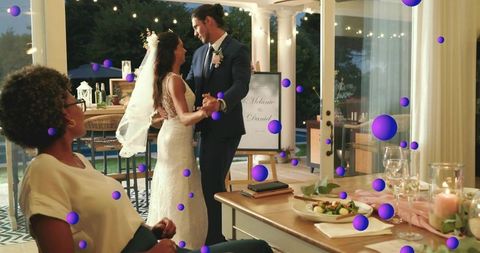 Newlyweds dancing under string lights on candlelit veranda at evening wedding reception