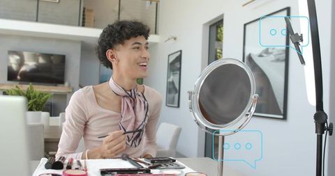 Smiling asian makeup creator demonstrating beauty routine at vanity with ring light