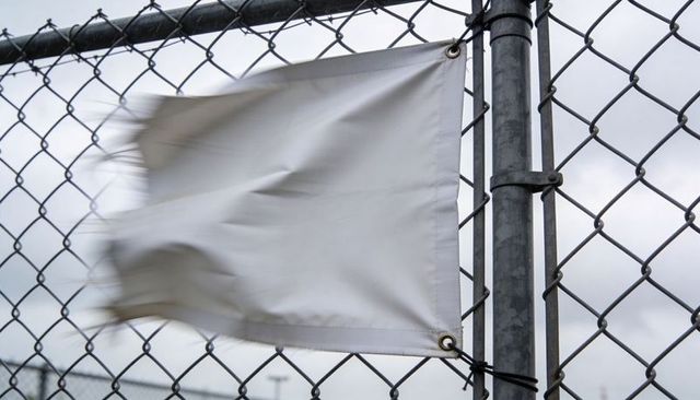Blank white banner billowing on chain-link fence with zip ties in windy overcast lot