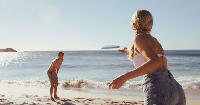 Couple enjoying a fun game of frisbee on a sunlit beach by the ocean, perfect for illustrating outdoor leisure activities, summer vacations, and healthy lifestyles.