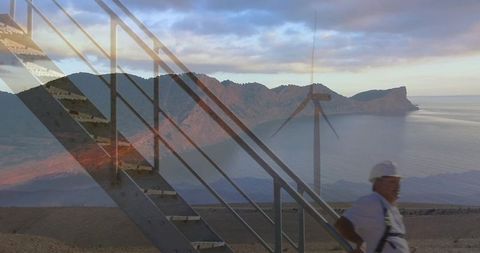 Wind farm technician climbing stairway wearing hard hat harness overlooking coastal turbine