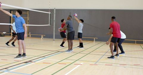 Diverse male teens practicing volleyball drills at indoor gym court focusing on teamwork