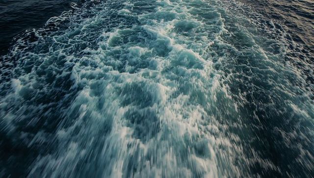 Boat wake churning across deep blue ocean surface with foamy turbulent motion and spray