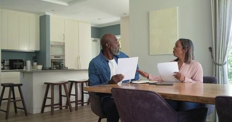 Diverse senior couple reviewing finances and documents at modern open-plan kitchen dining table