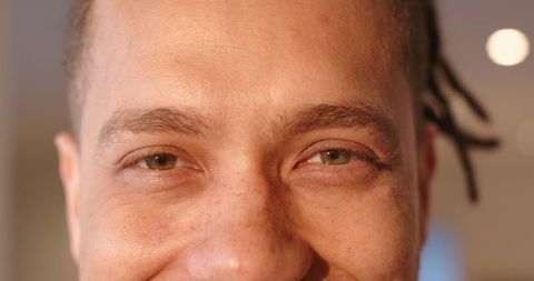 Mid-adult man gazing and smiling close-up with freckles and braided hair, warm skin texture