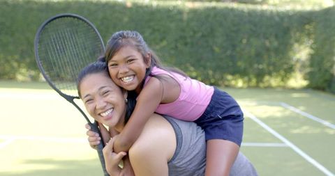 Happy Mother Carrying Daughter on Tennis Court Showing Bonding