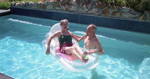 Senior couple relaxing on inflatable lounger in sunny backyard pool