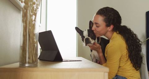 Caucasian woman kissing dog while using tablet at home