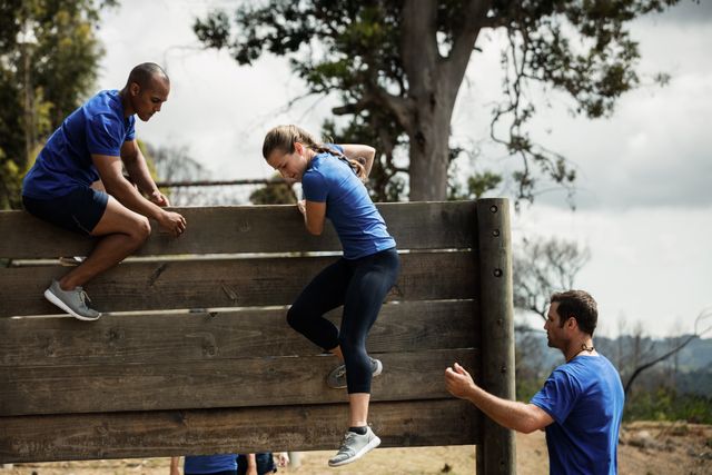 Male trainer assisting woman to climb a wooden wall during obstacle course