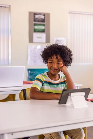 Smiling african american schoolboy using tablet for digital learning in modern classroom
