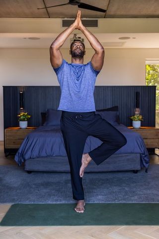 Mature african american man practicing tree pose in bedroom for yoga and mindfulness
