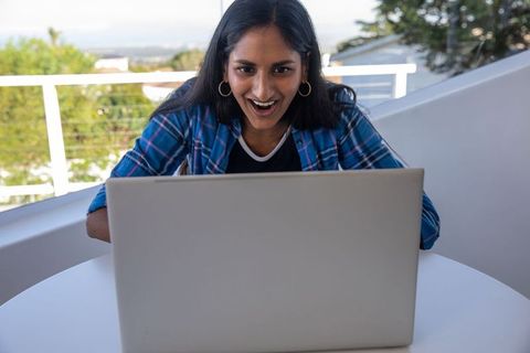 Excited Woman Sitting on Balcony Using Laptop Outdoors