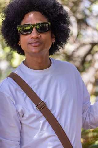 African american man wearing sunglasses and crossbody strap posing in sunlit park
