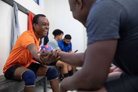 Smiling african american volleyball teammates shaking hands in locker room