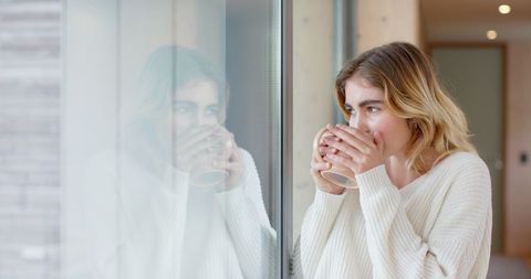 Woman Reflecting Through Window Holding Mug in Cozy Home