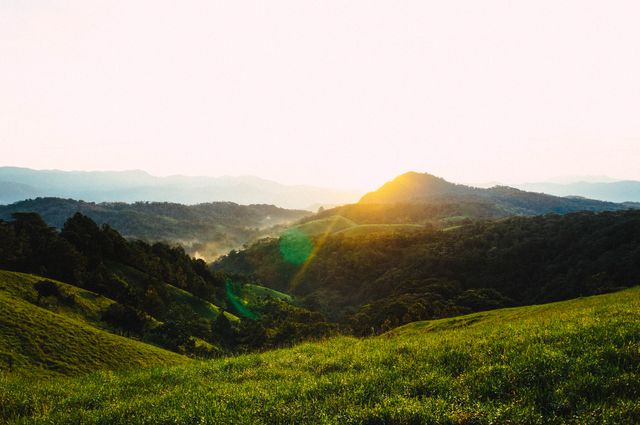 Scenic sunrise over lush green mountains with mist in the valleys. This is a great image for use in travel brochures, outdoor adventure advertisements, or nature-themed blogs and websites. Perfect for conveying a sense of serenity and the untouched beauty of nature.
